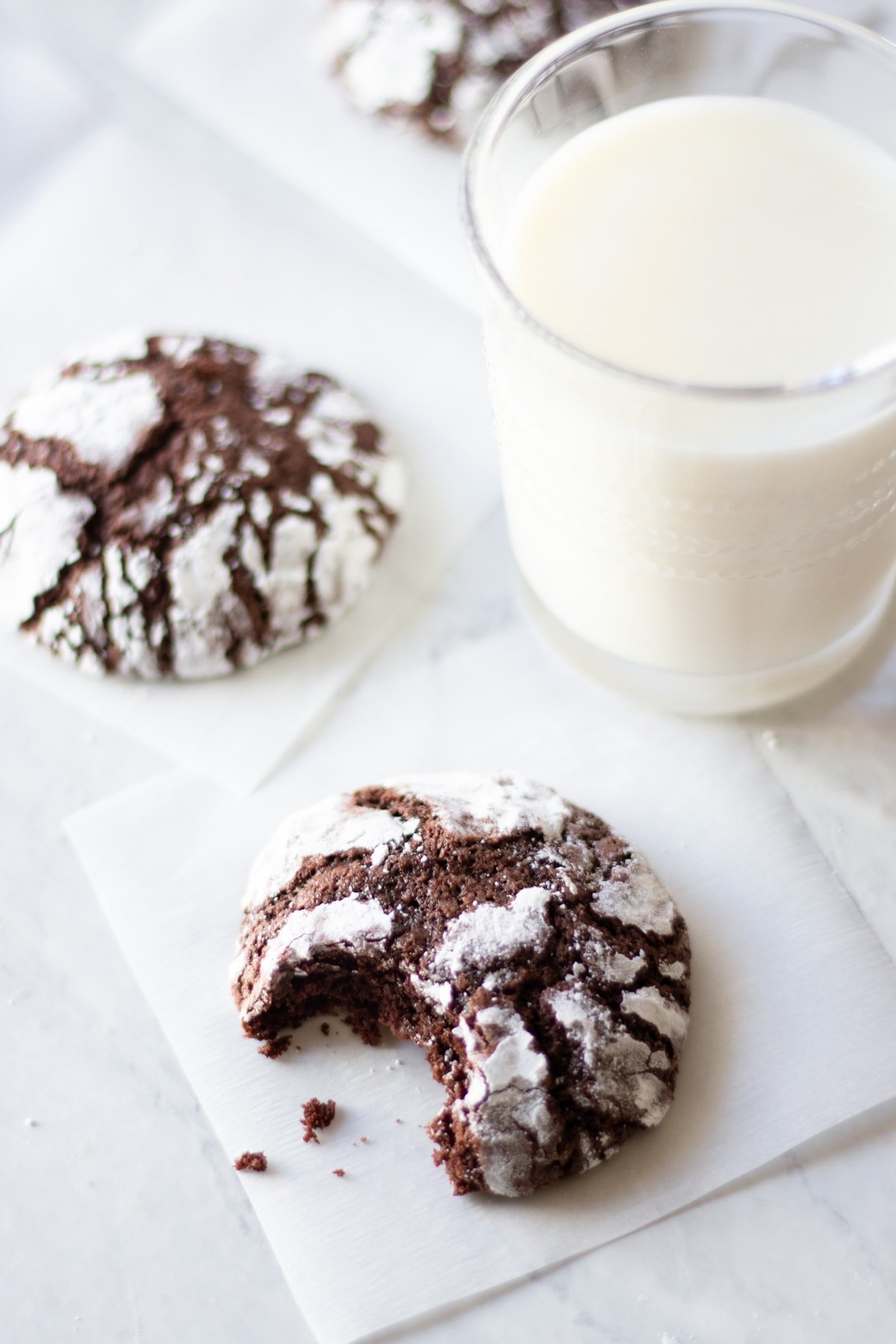 A cocoa crinkle cookie with a bite taken out sitting next to a glass of milk.