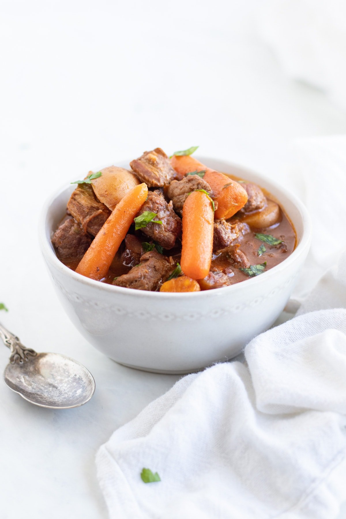 A bowl of low FODMAP beef stew surrounded by a white cloth napkin and antique spoon.