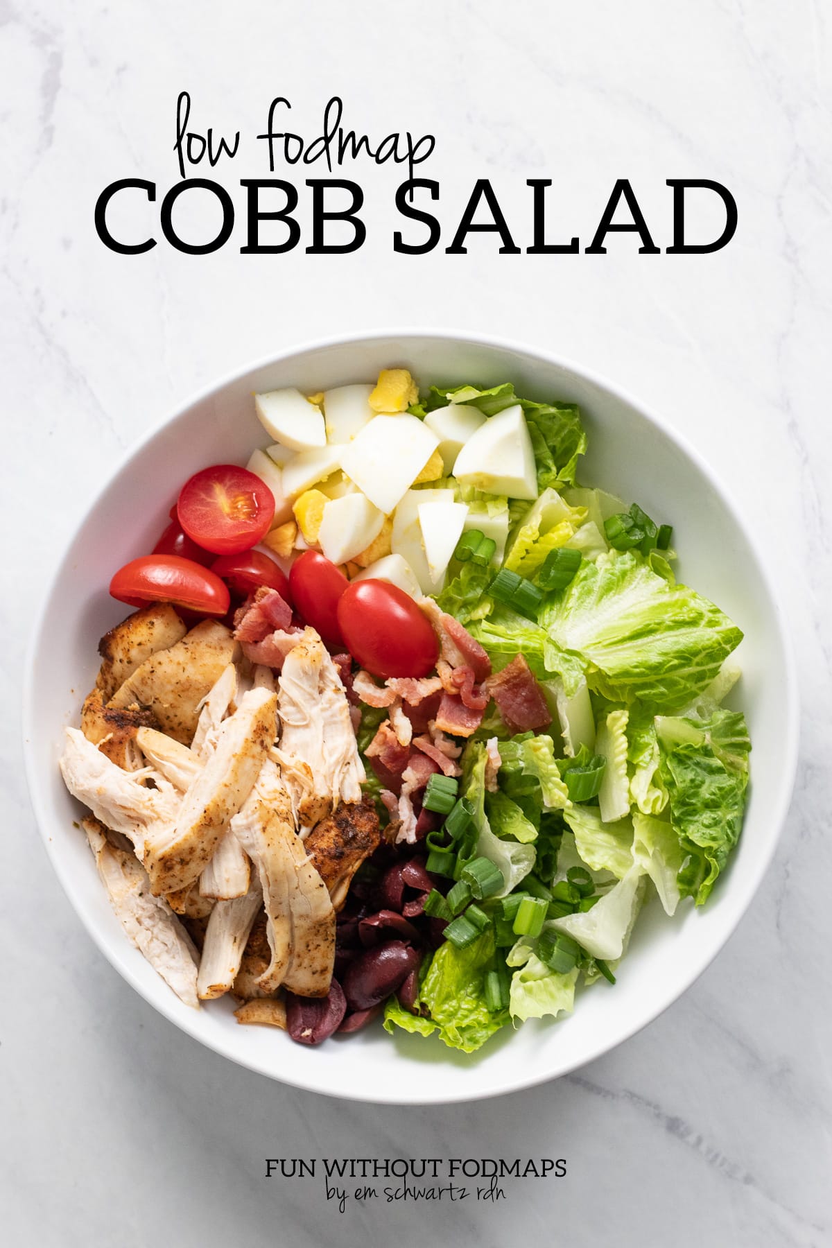 A bowl filled with lettuce, bacon, chicken, hard-boiled eggs, cherry tomatoes, and kalamata olives.  Above the bowl, black text reads "Low FODMAP Cobb Salad."