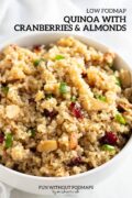 Quinoa salad dotted with green onion tops, dried cranberries, and toasted almonds. In the white space above text reads "Low FODMAP Quinoa with Cranberries and Almonds."