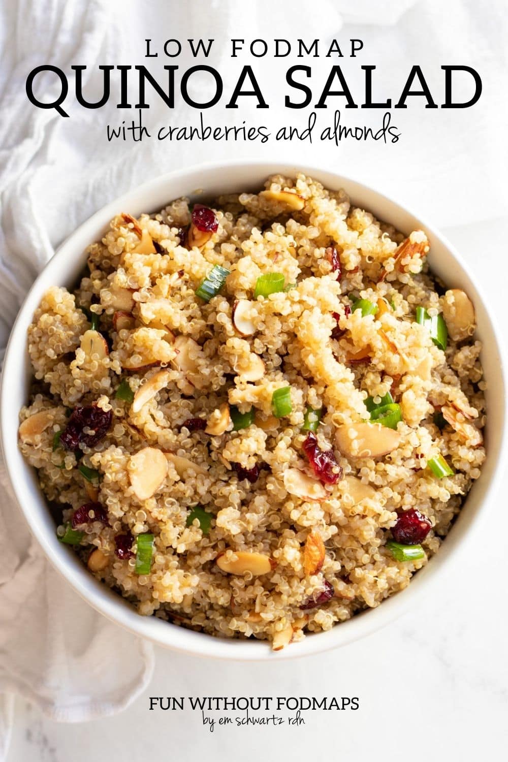 A bowl of quinoa salad dotted with toasted almonds and dried cranberries. In the white space above the bowl, a black text overlay reads "Low FODMAP Quinoa Salad with Cranberries and Almonds."