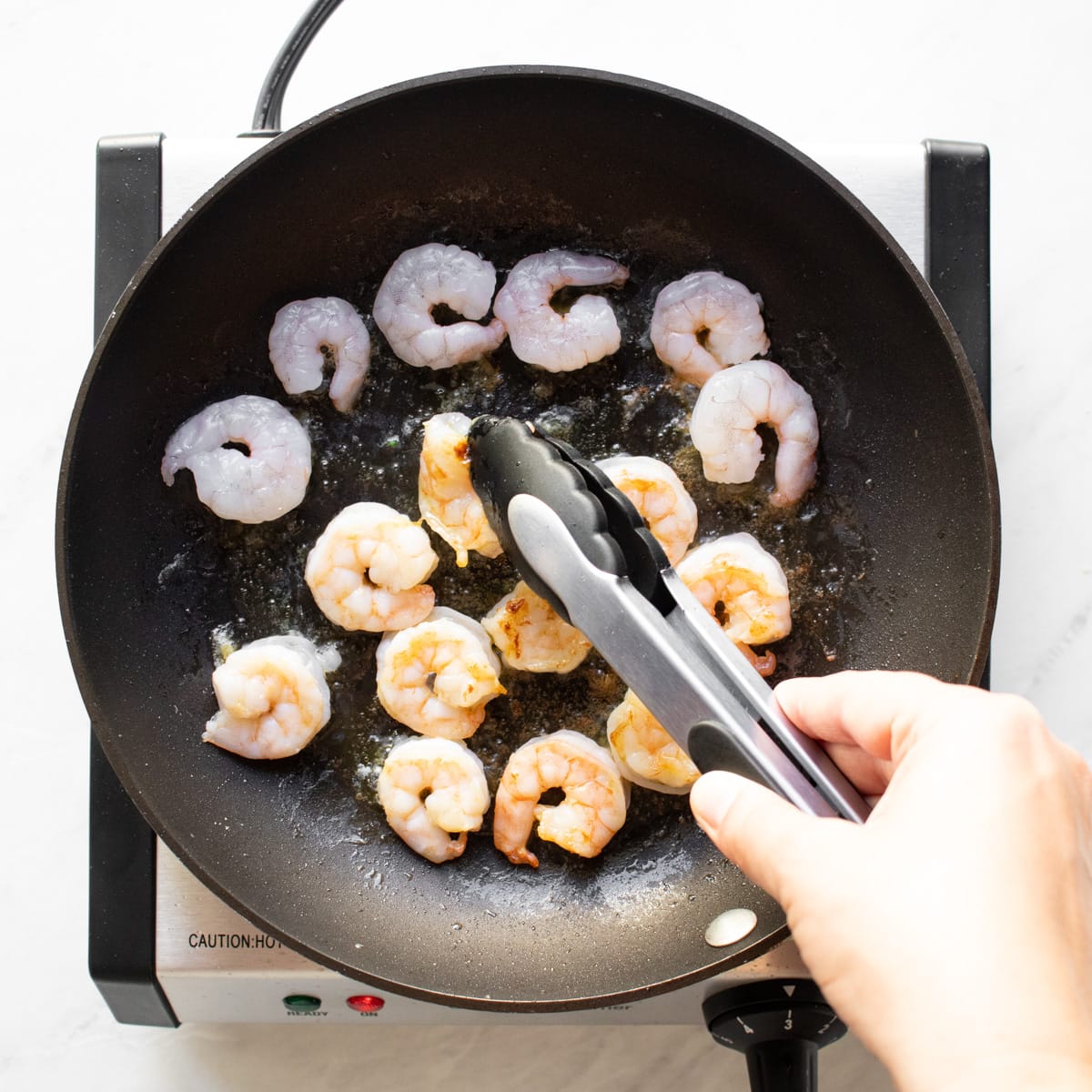 Flipping shrimp with a tongs to cook evenly on both sides.