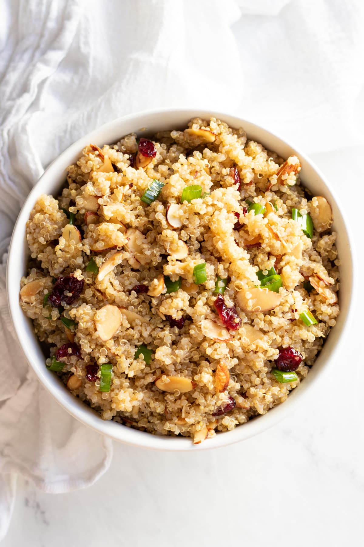 A bowl of quinoa salad dotted with dried cranberries, toasted sliced almonds, and green onion tops.