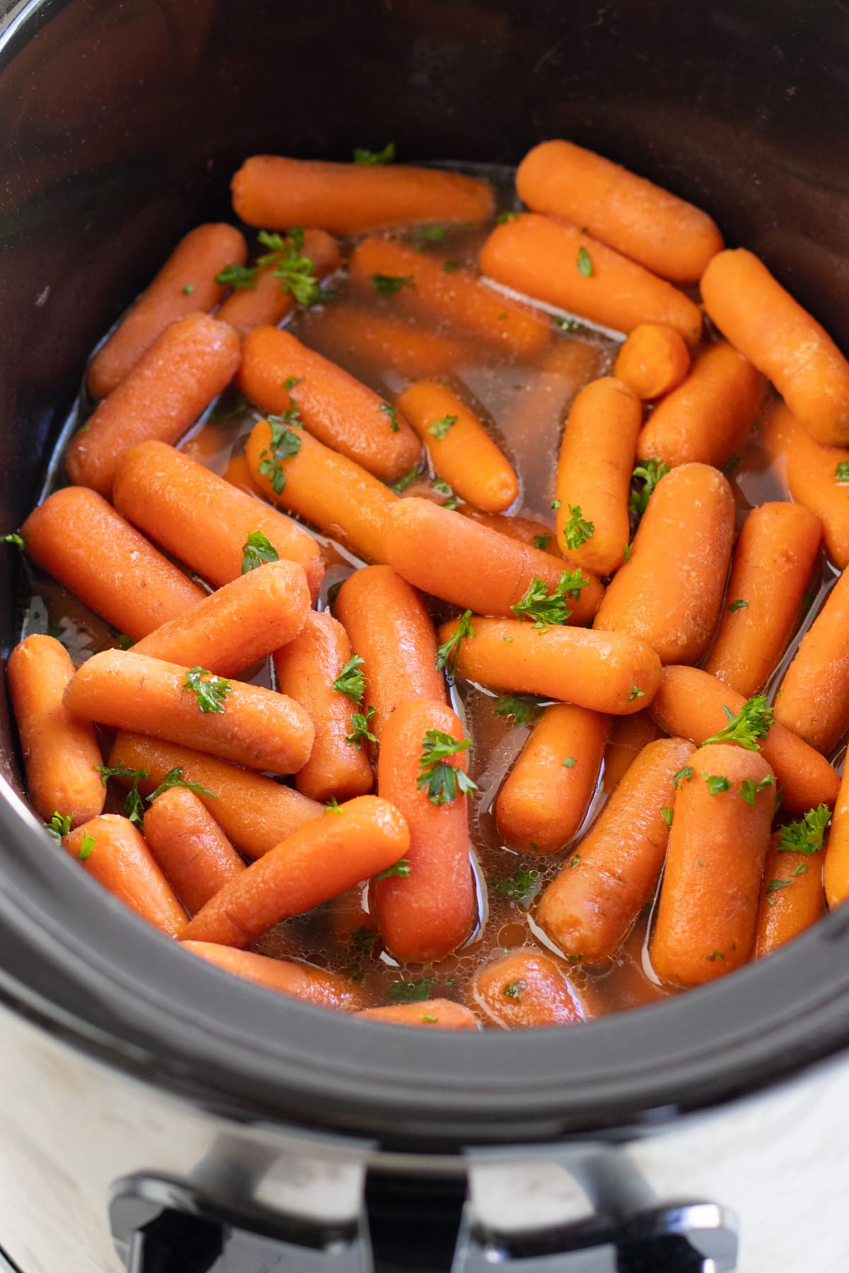 Cooked carrots topped with fresh parsley in a slow cooker 
