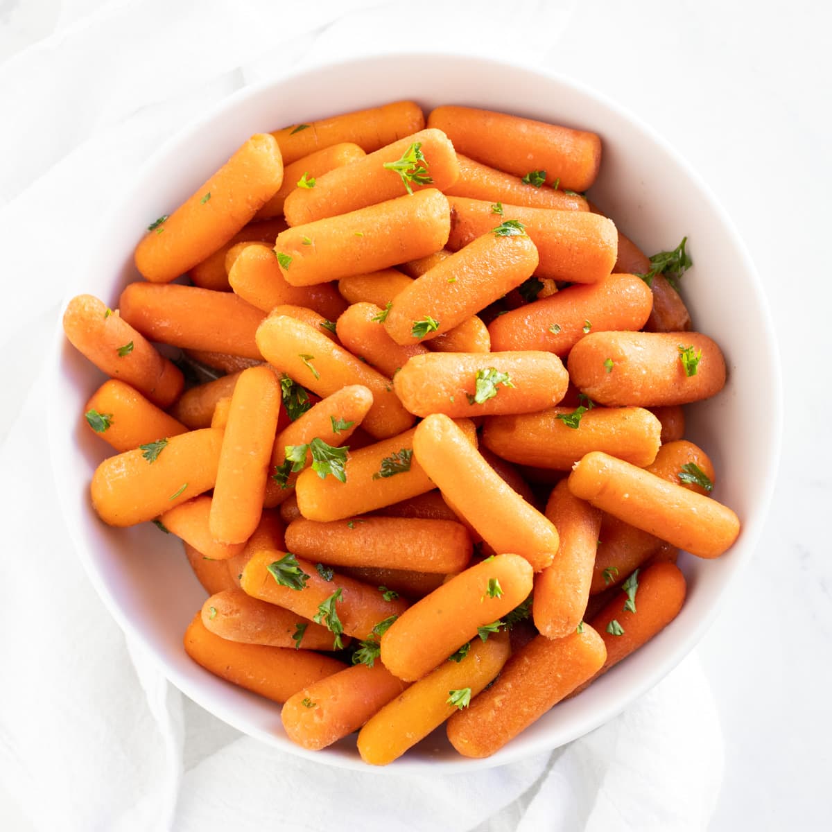 A bowl of cooked carrots topped with chopped fresh parsley.
