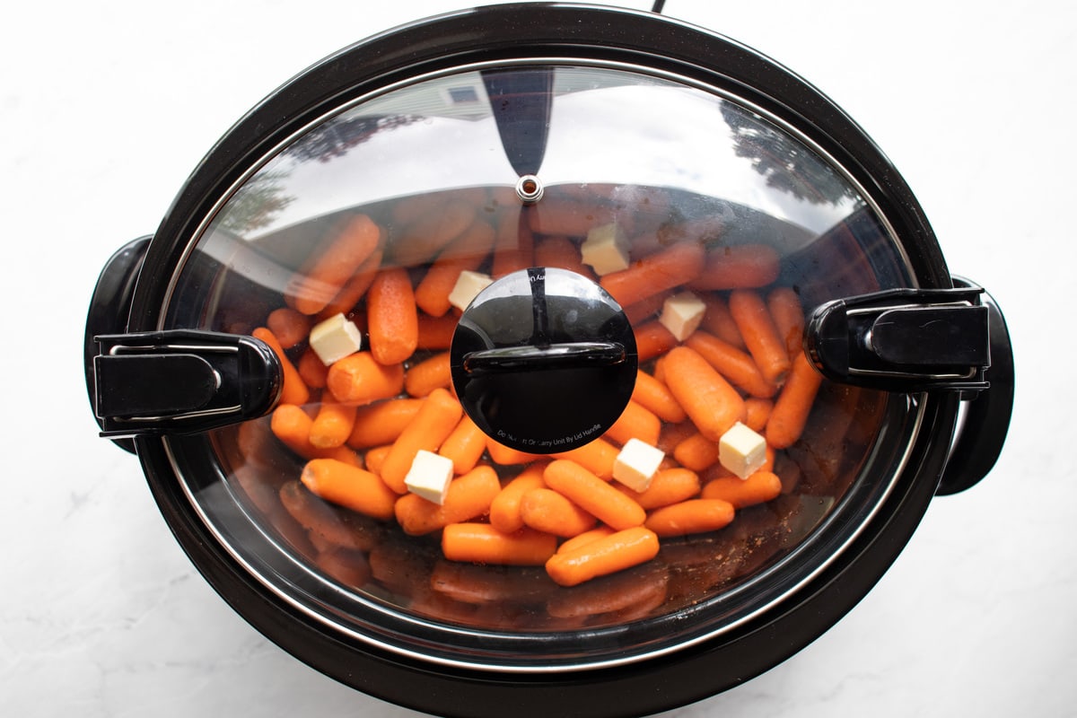Uncooked carrots in a slow cooker with a lid.