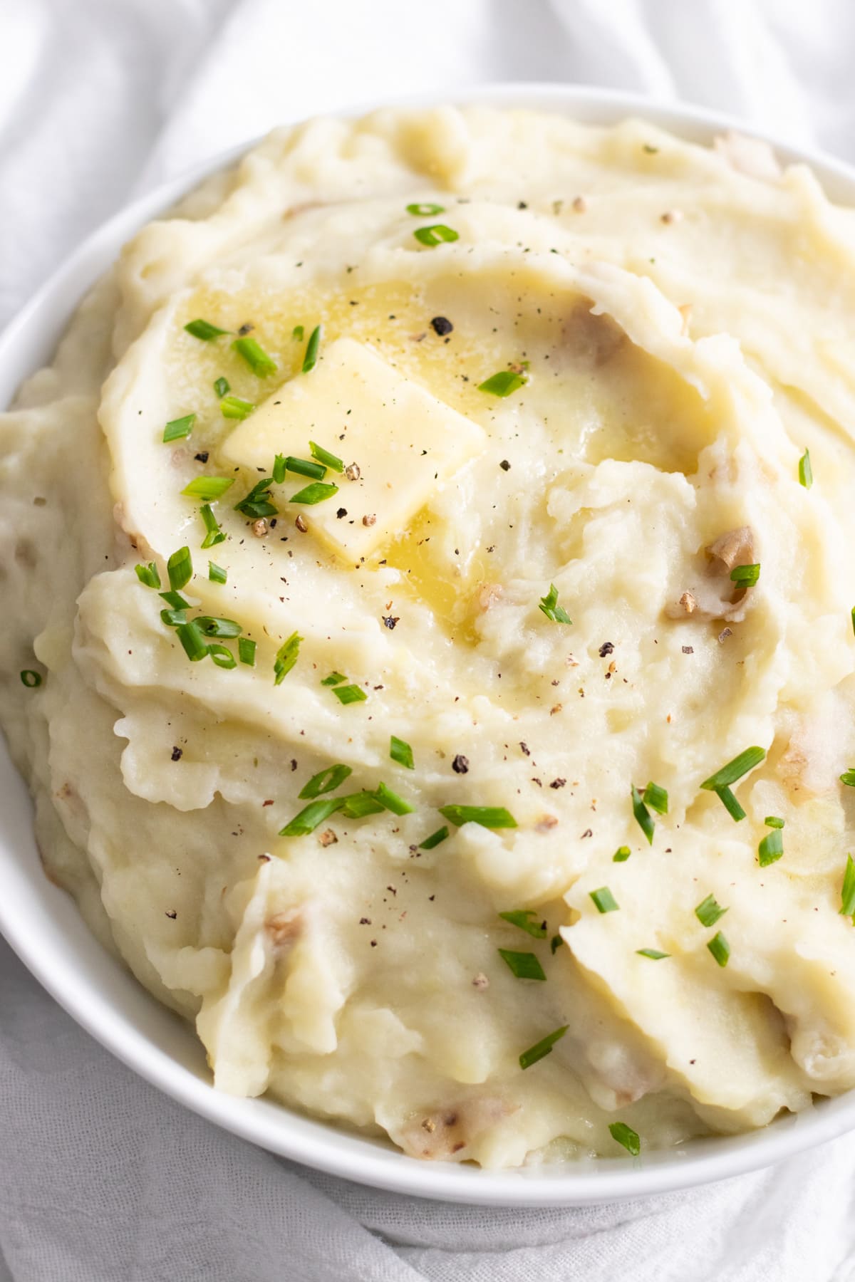 A close up of creamy mashed potatoes topped with a dab of butter, snipped chives, and black pepper.