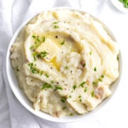 A bowl of rustic mashed potatoes topped with a pat of butter, snipped chives, and fresh cracked black pepper.