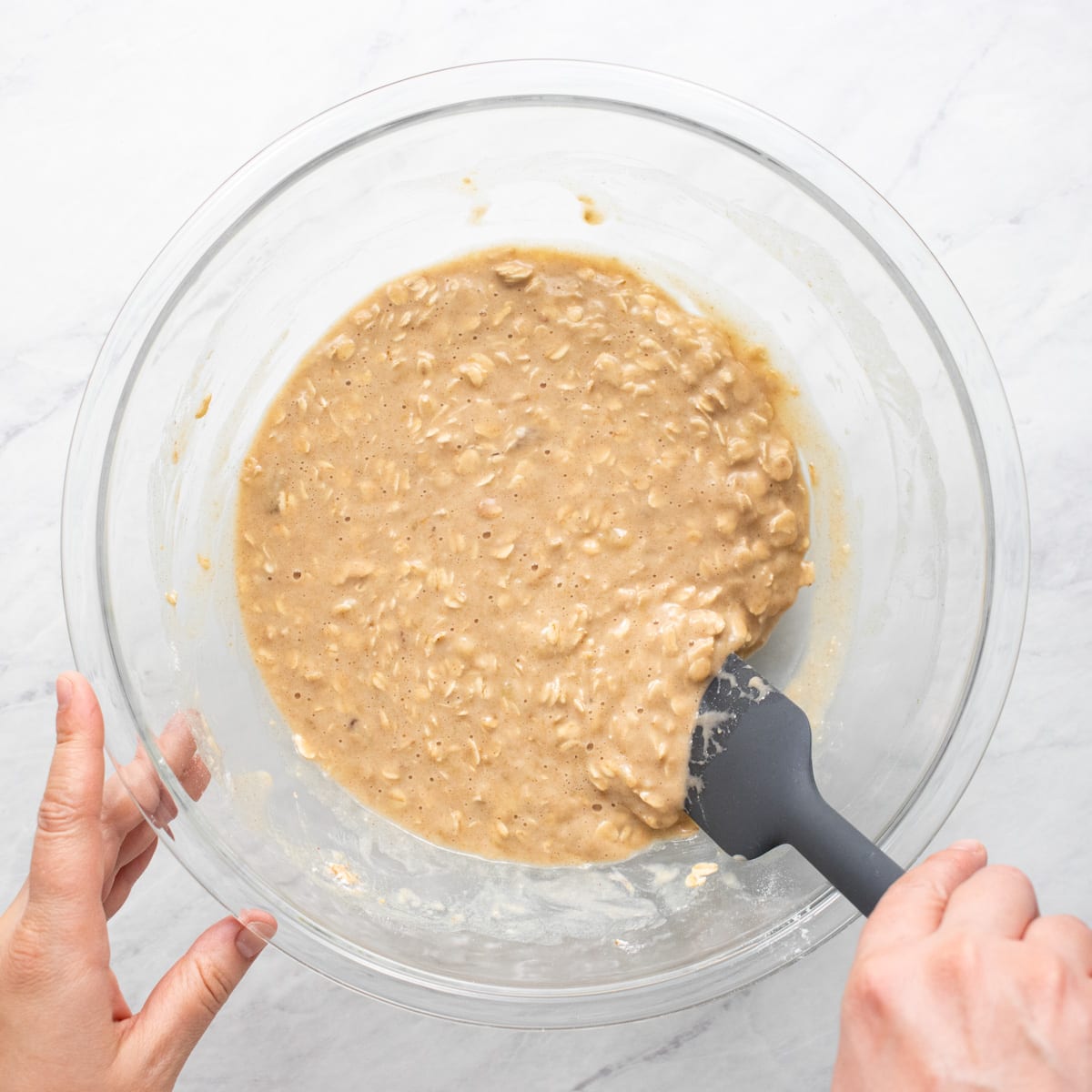 The side of the bowl containing the batter is being scraped with a spatula to get any lingering unmixed ingredients.