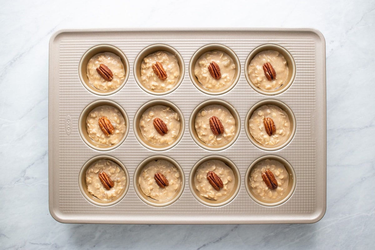 Each batter-filled muffin tin cup is topped with a pecan halve.