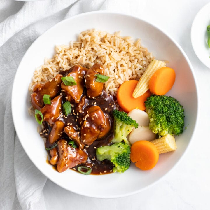 A bowl of low FODMAP sesame chicken, steamed mixed veggies, and brown rice