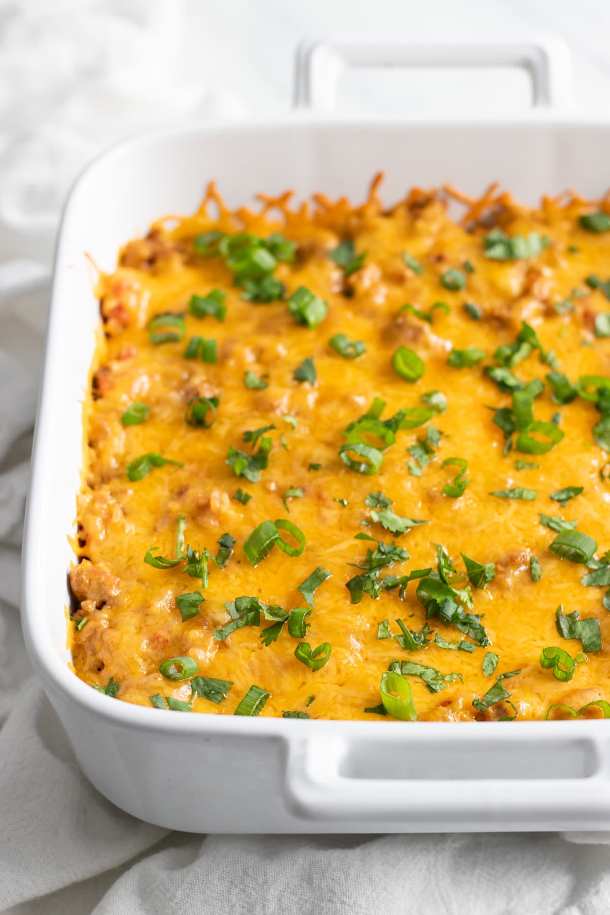 A close up of a cheesy casserole topped with sliced green onion tops and fresh cilantro.
