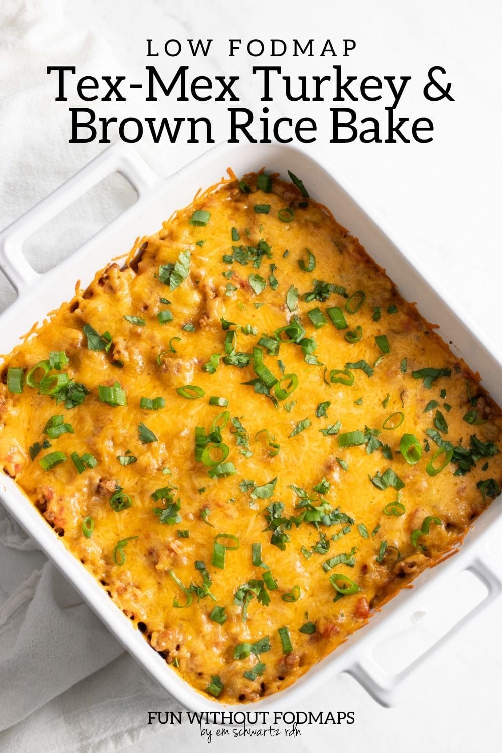 A white baking dish with a cheesy casserole topped with sliced green onion tops and chopped cilantro. In the white space above, black text reads "Low FODMAP Tex-Mex Turkey and Brown Rice Bake."