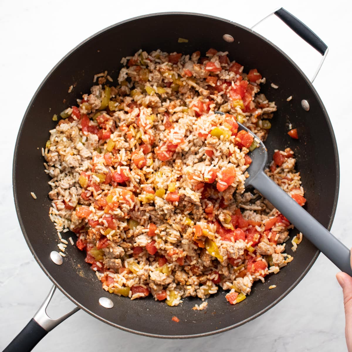 Brown rice, canned tomatoes, diced chiles, and spices added to browned ground turkey in skillet.