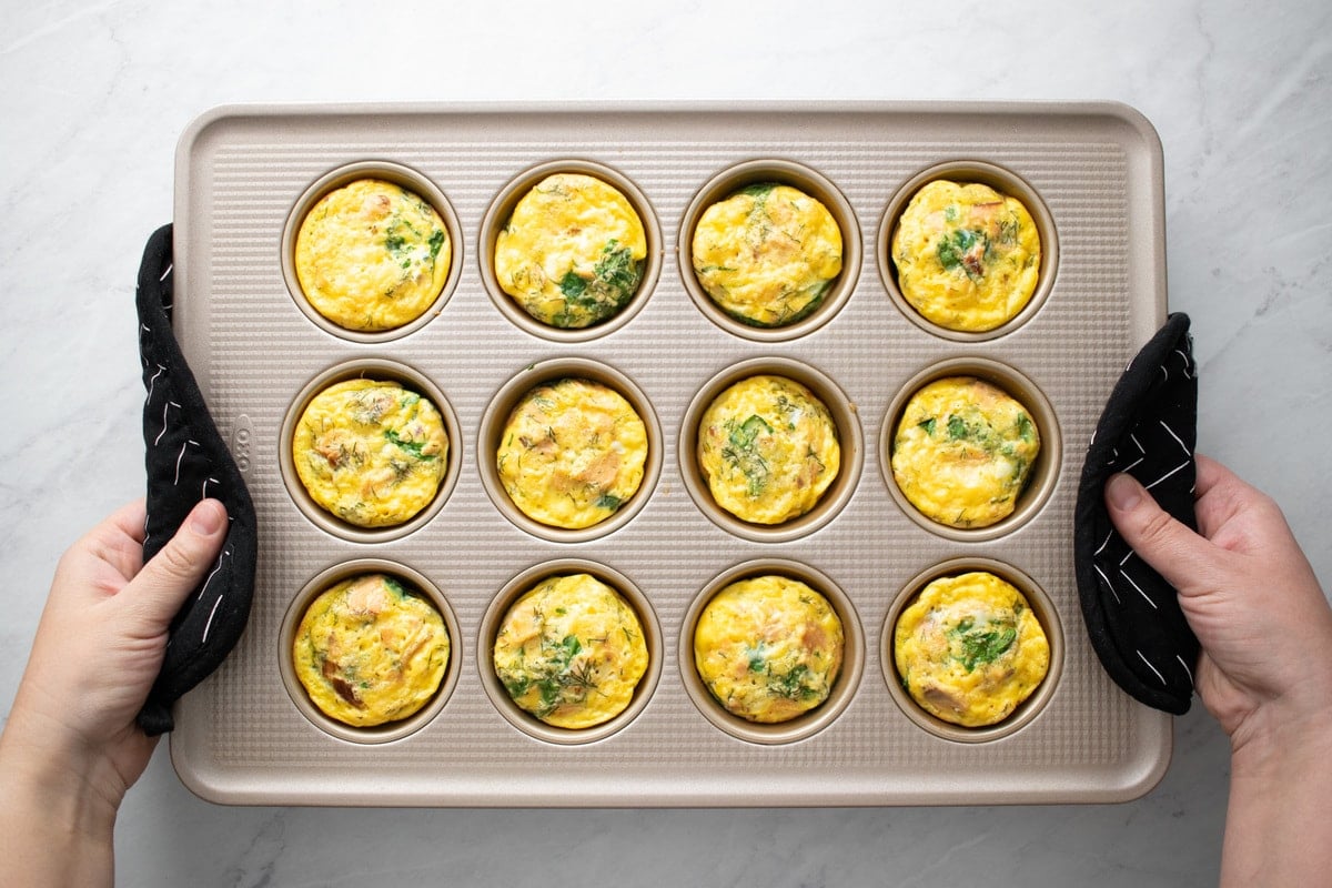 Holding a muffin tin filled with baked smoked salmon and spinach egg muffins.