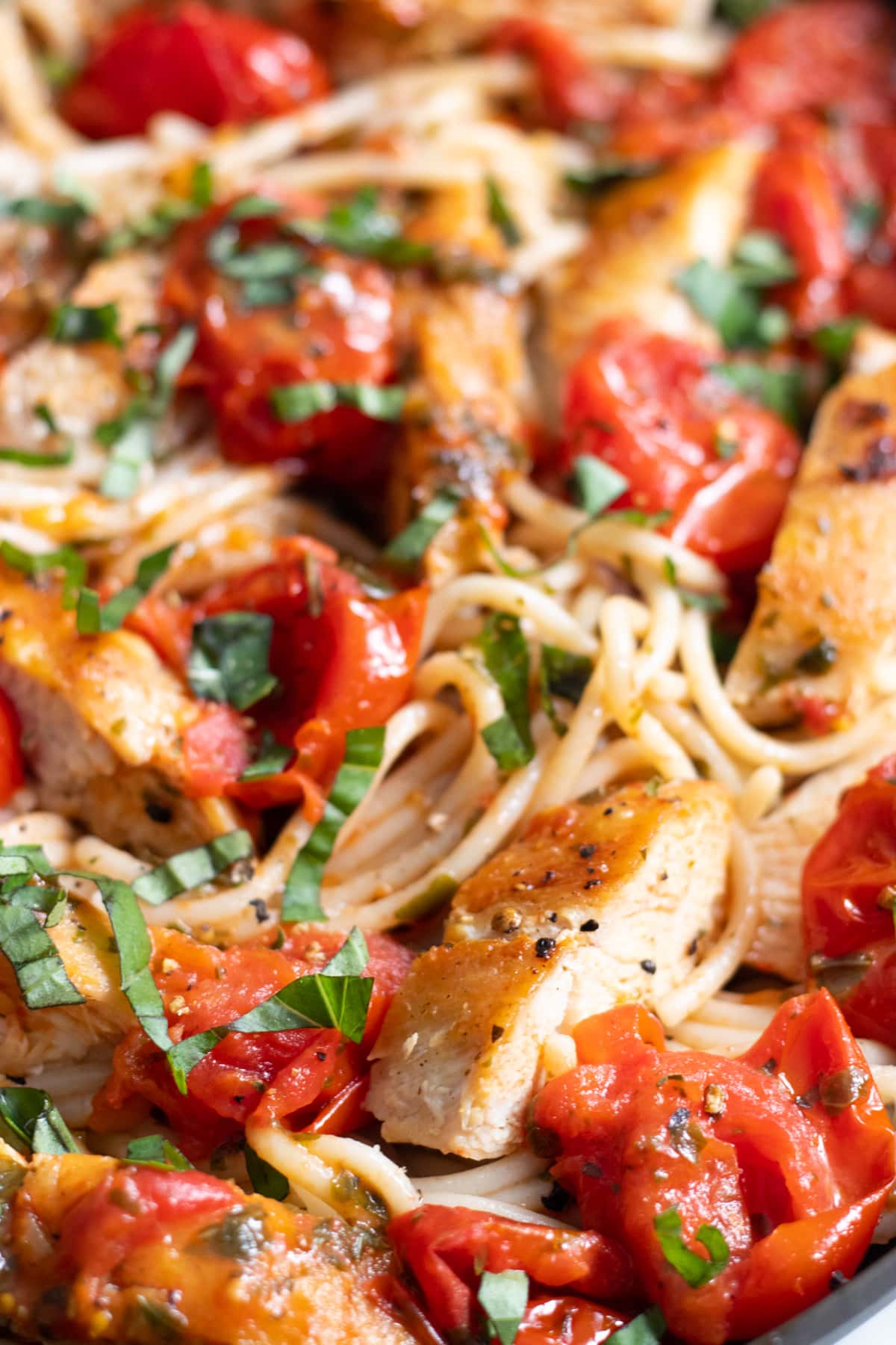 Cooked spaghetti mixed with pan-fried chicken slices, burst cherry tomatoes, and freshly sliced basil.
