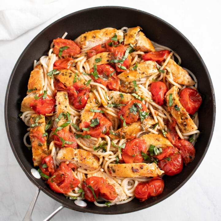 A skillet filled with spaghetti, crushed cherry tomatoes, and cooked chicken slices.