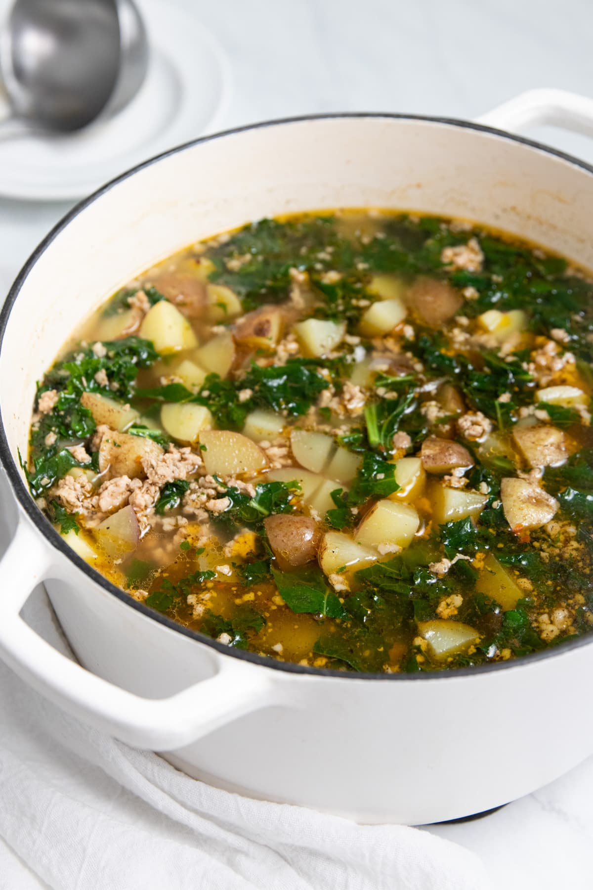 Looking into a soup-filled Dutch oven. The soup is made with diced potatoes, sausage crumbles and chopped kale.