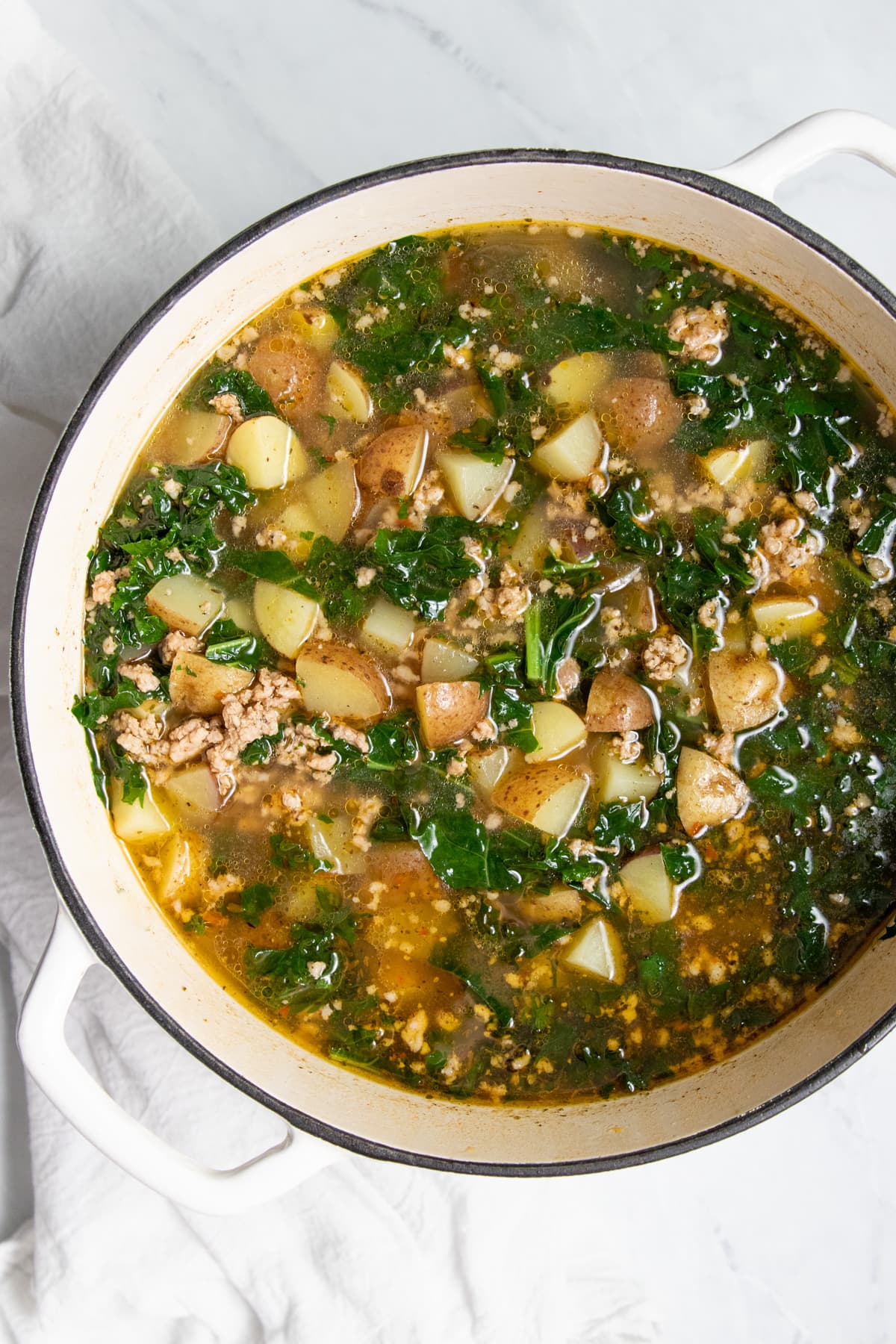 Looking down at a pot filled with a soup made with potatoes, kale, and sausage