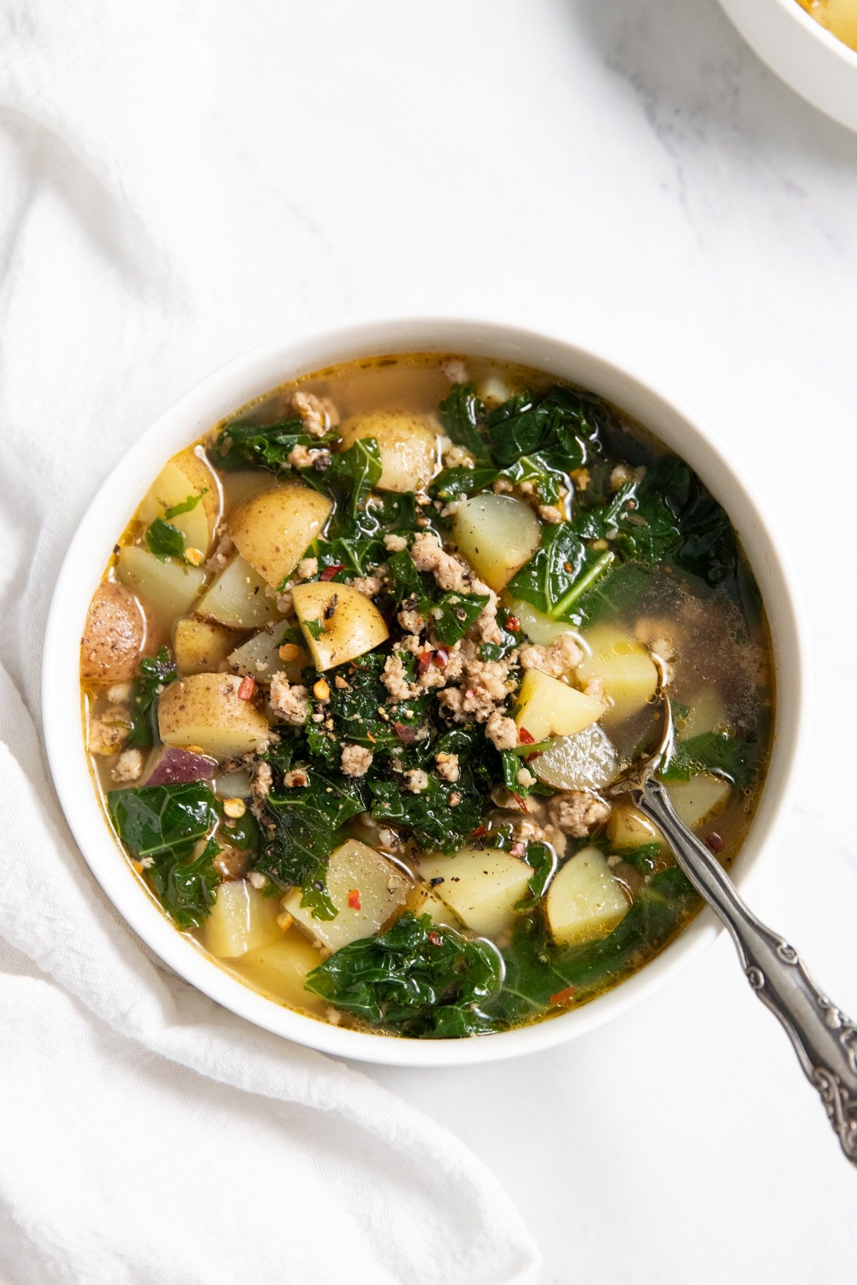 A bowl of kale, potato, and sausage soup with a spoon in it.