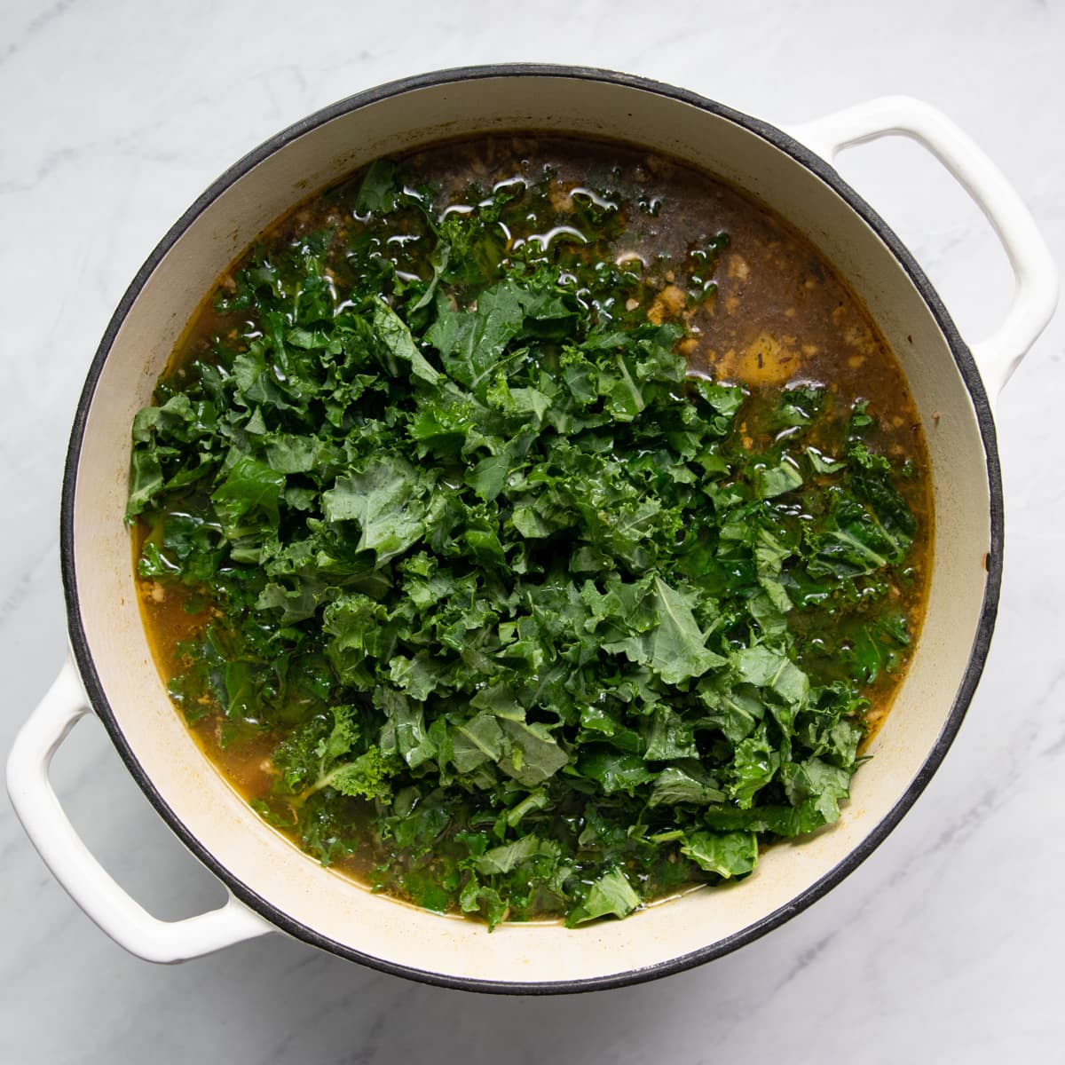 Chopped kale has been placed on the top of soup cooked in a Dutch oven.