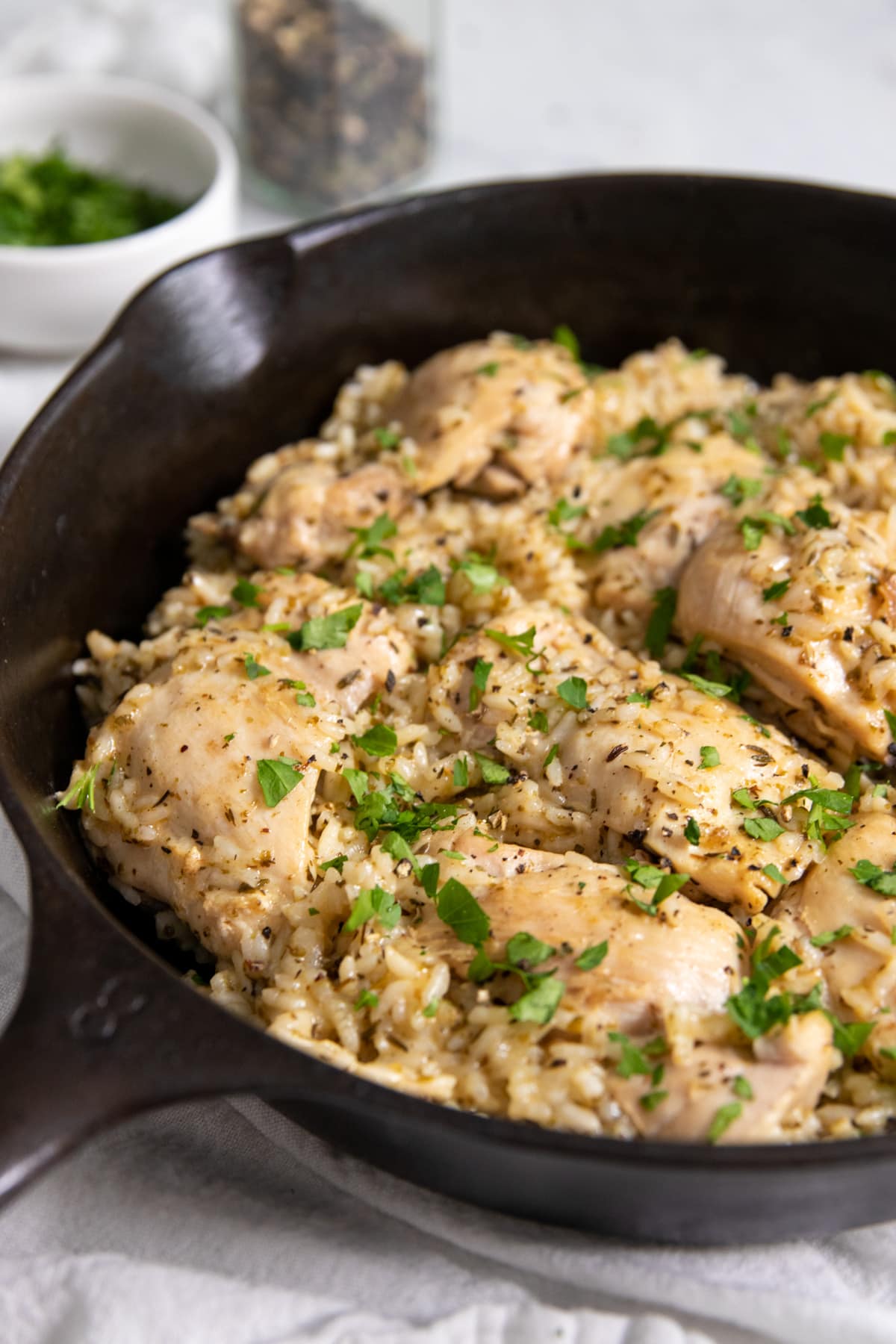 Looking into a pan of cooked chicken and rice. Everything is flavored with visible dried Italian herbs and there is an abundance of chopped fresh parsley sprinkled on top.