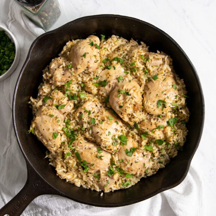 A skillet full of lemon chicken and rice topped with chopped parsley