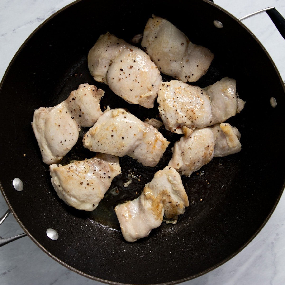 Lightly browned and seasoned boneless, skinless chicken thighs are in a non-stick skillet.