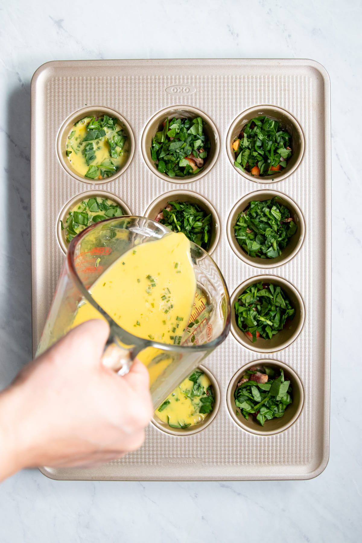 Pouring whisked egg into veggie-filled muffin tins. 