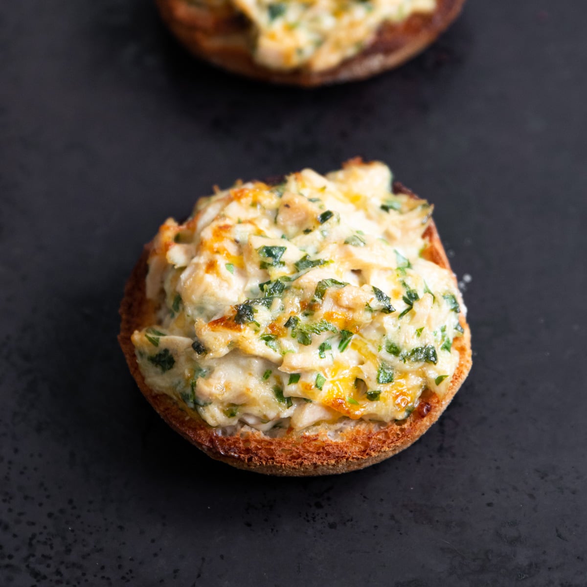 An English muffin half topped with a cheesy tuna salad that has been melted under a broiler.
