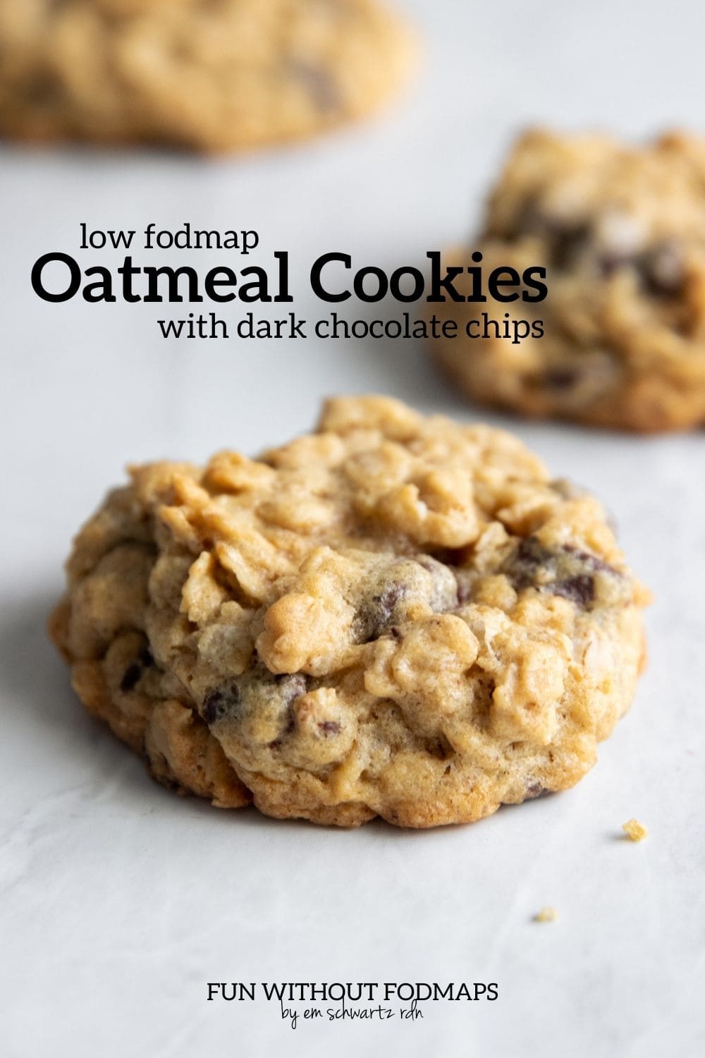 Three cookies on a marble counter. A black text overlay reads "low FODMAP oatmeal cookies with dark chocolate chips".