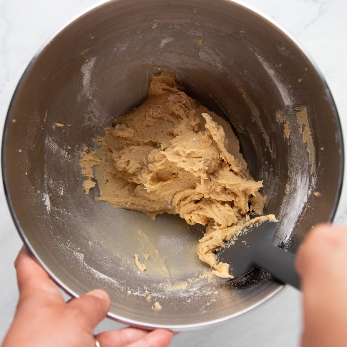 Scraping the sides of a mixing bowl filled with cookie dough.