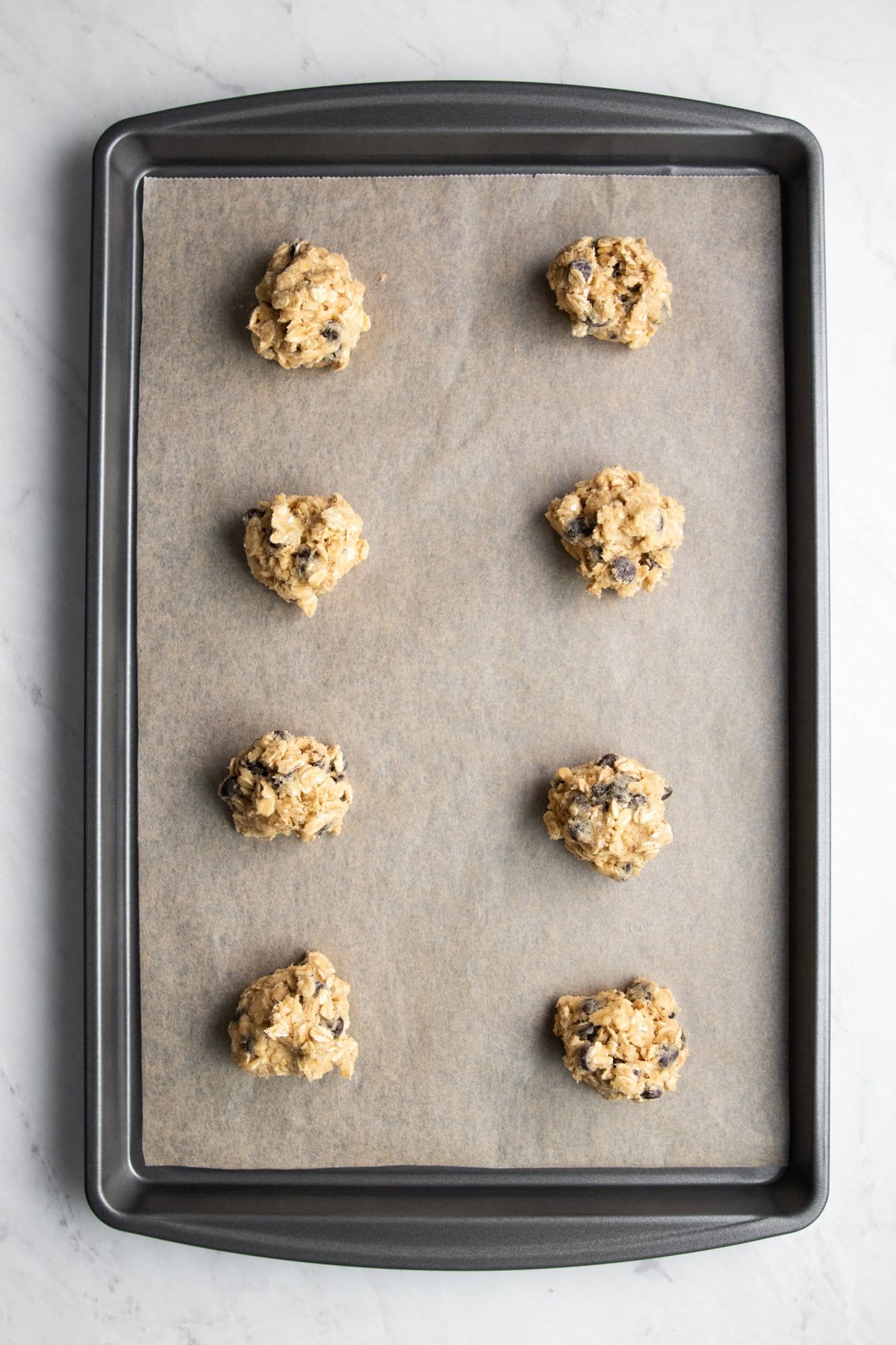 Eight cookie dough balls on a baking sheet lined with parchment paper.