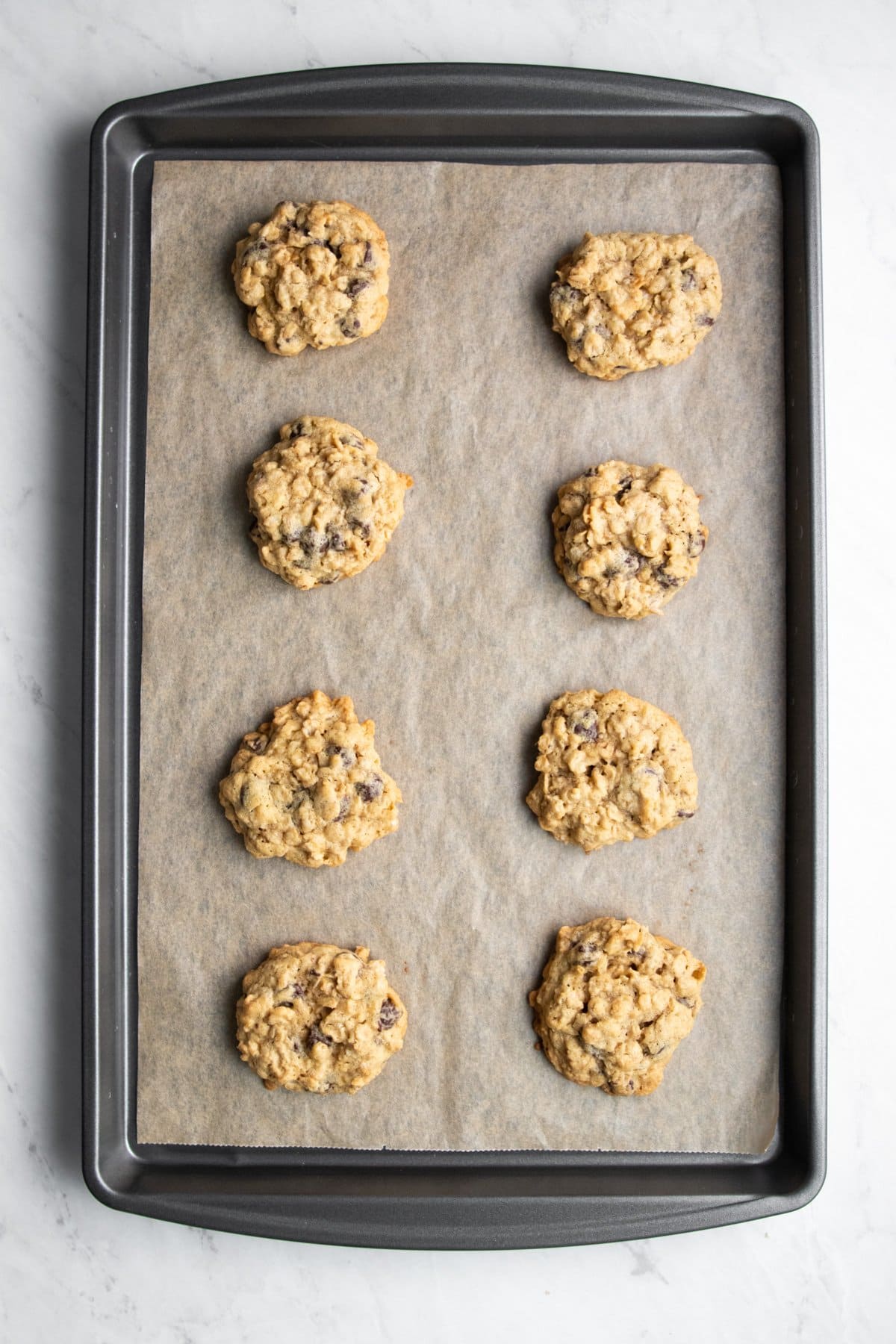 Eight baked low FODMAP oatmeal chocolate chip cookies on a baking sheet lined with parchment paper.