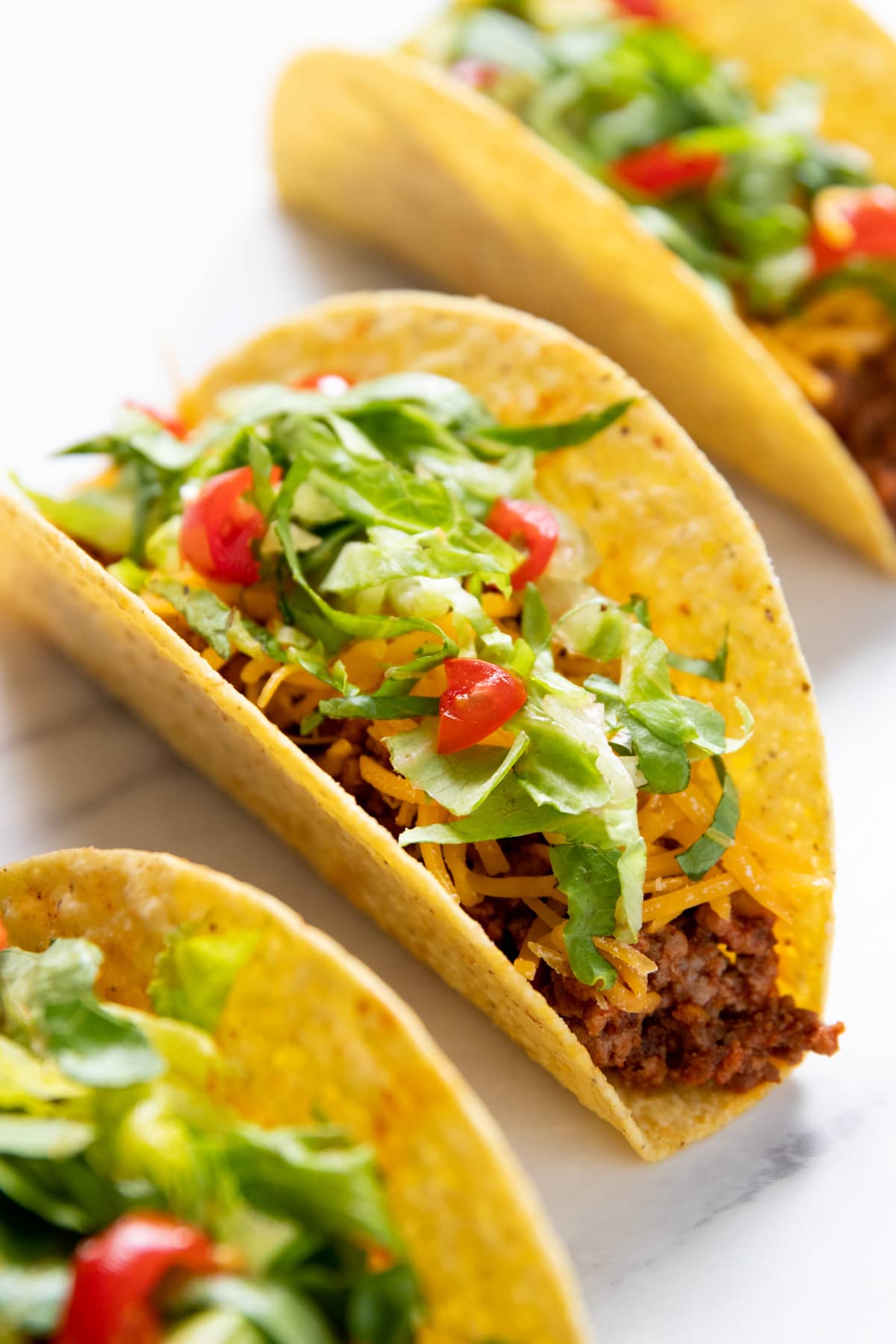 Three hard shell tacos filled with low FODMAP ground beef taco meat, shredded cheddar, shredded lettuce, and diced cherry tomatoes. 