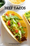 A hard shell taco on a rectangular plate. A black text overlay reads "Low FODMAP Beef Tacos".