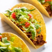 A hard shell taco filled with low FODMAP taco beef, shredded cheddar, shredded lettuce, and diced cherry tomatoes.