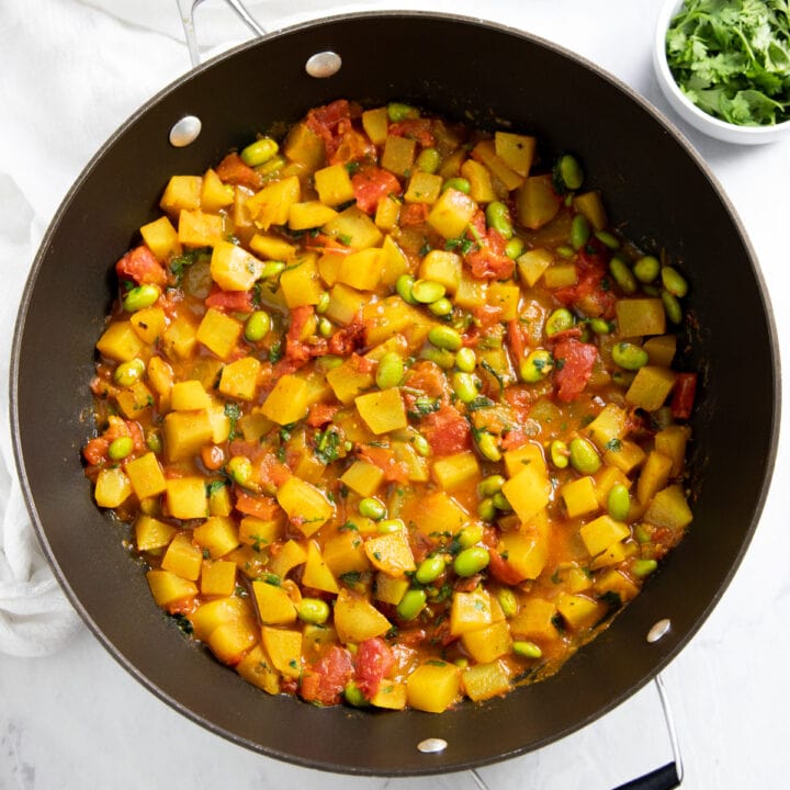 A skillet filled with a curry made with shelled edamame, tomatoes, and potatoes.