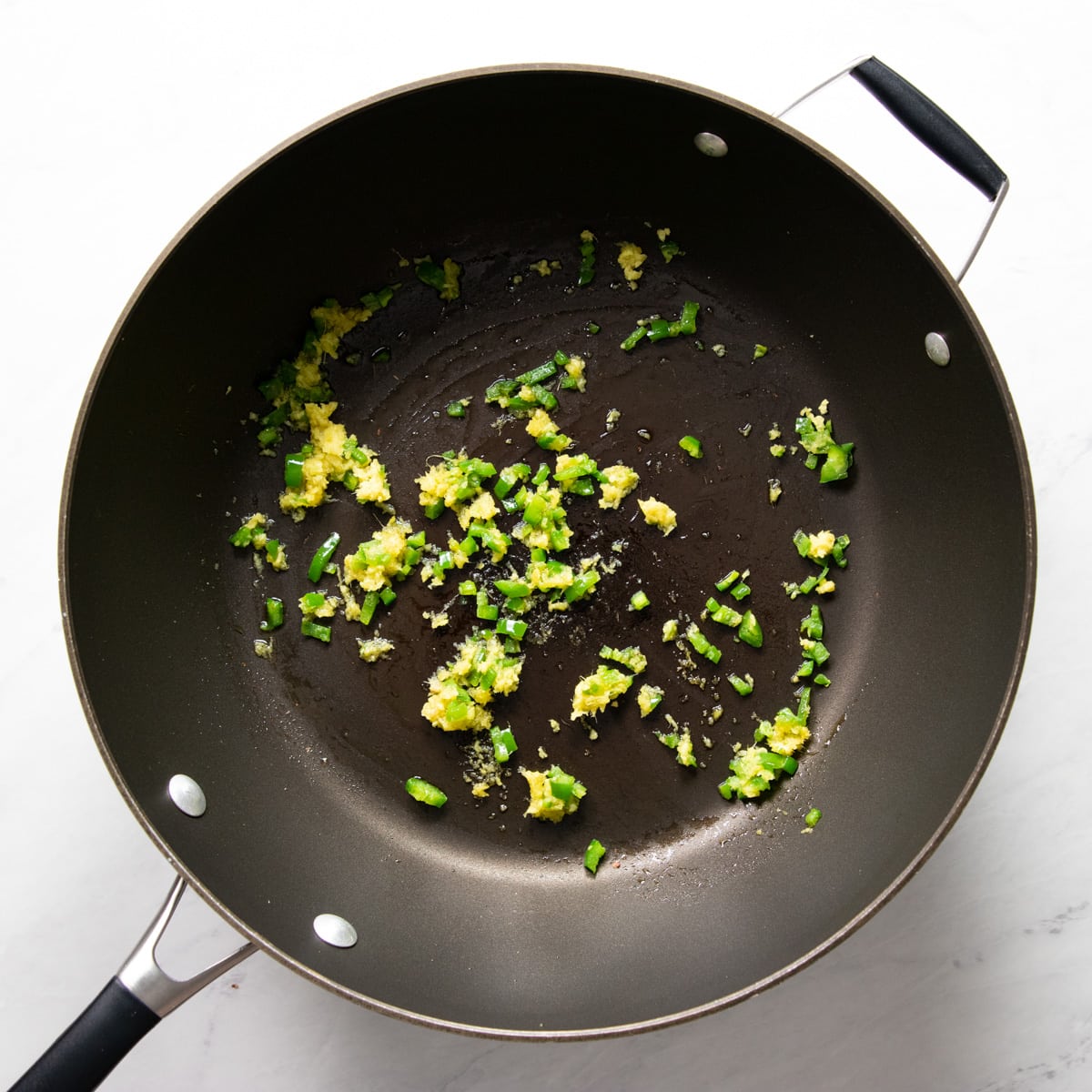 A skillet containing finely-chopped jalapeño and finely-grated fresh ginger sautéing in some garlic-infused oil.