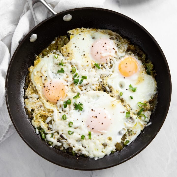A skillet filled with four cooked eggs sitting in a salsa verde sauce.