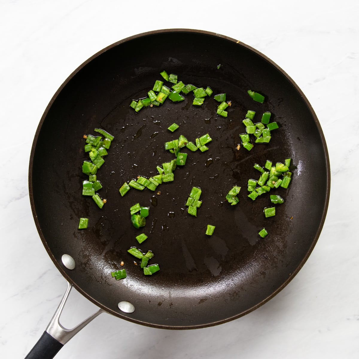 A skillet with oil and minced jalapeño.