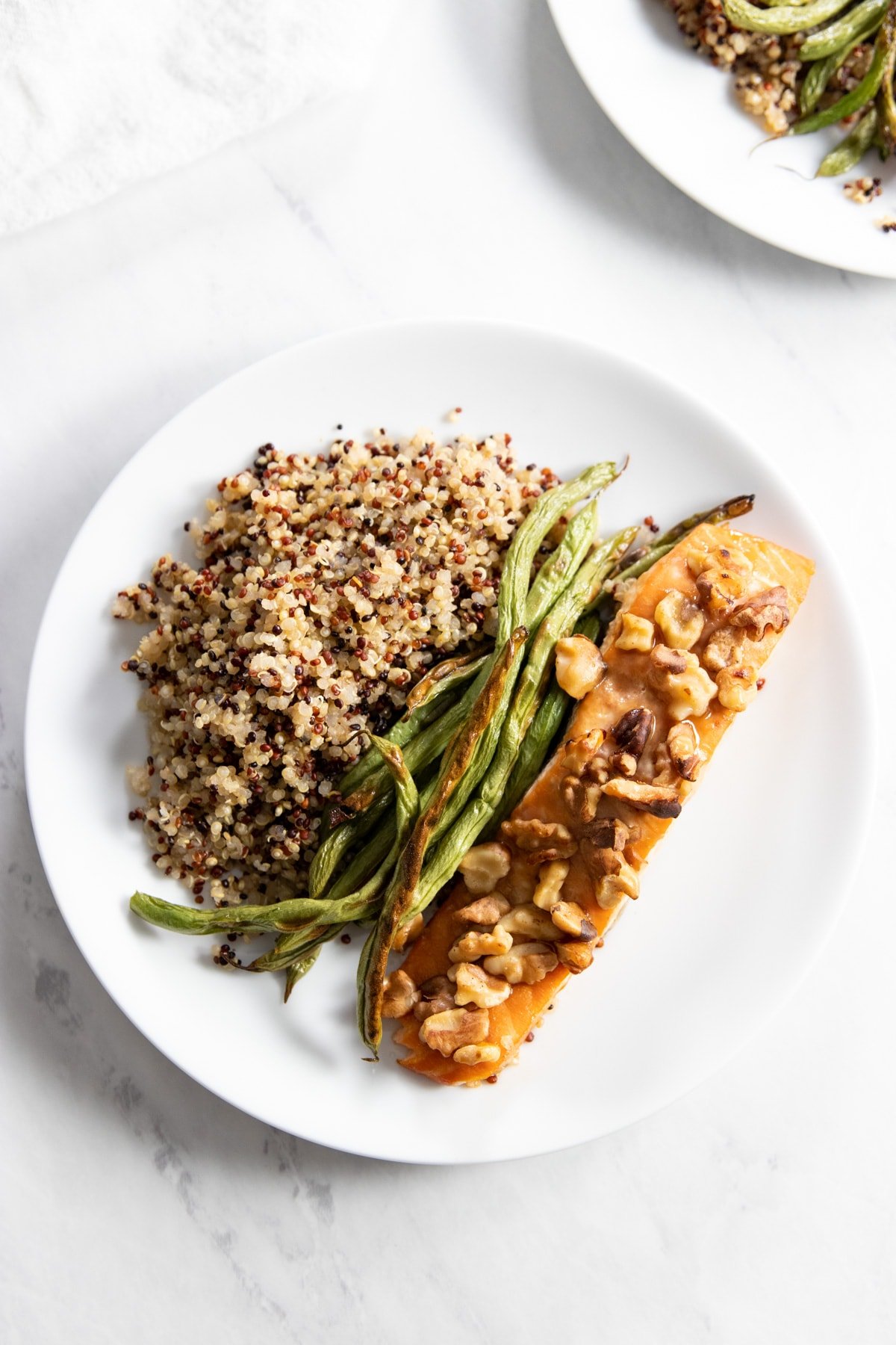 A plate containing walnut-topped salmon, roasted green beans, and cooked tri-color quinoa.