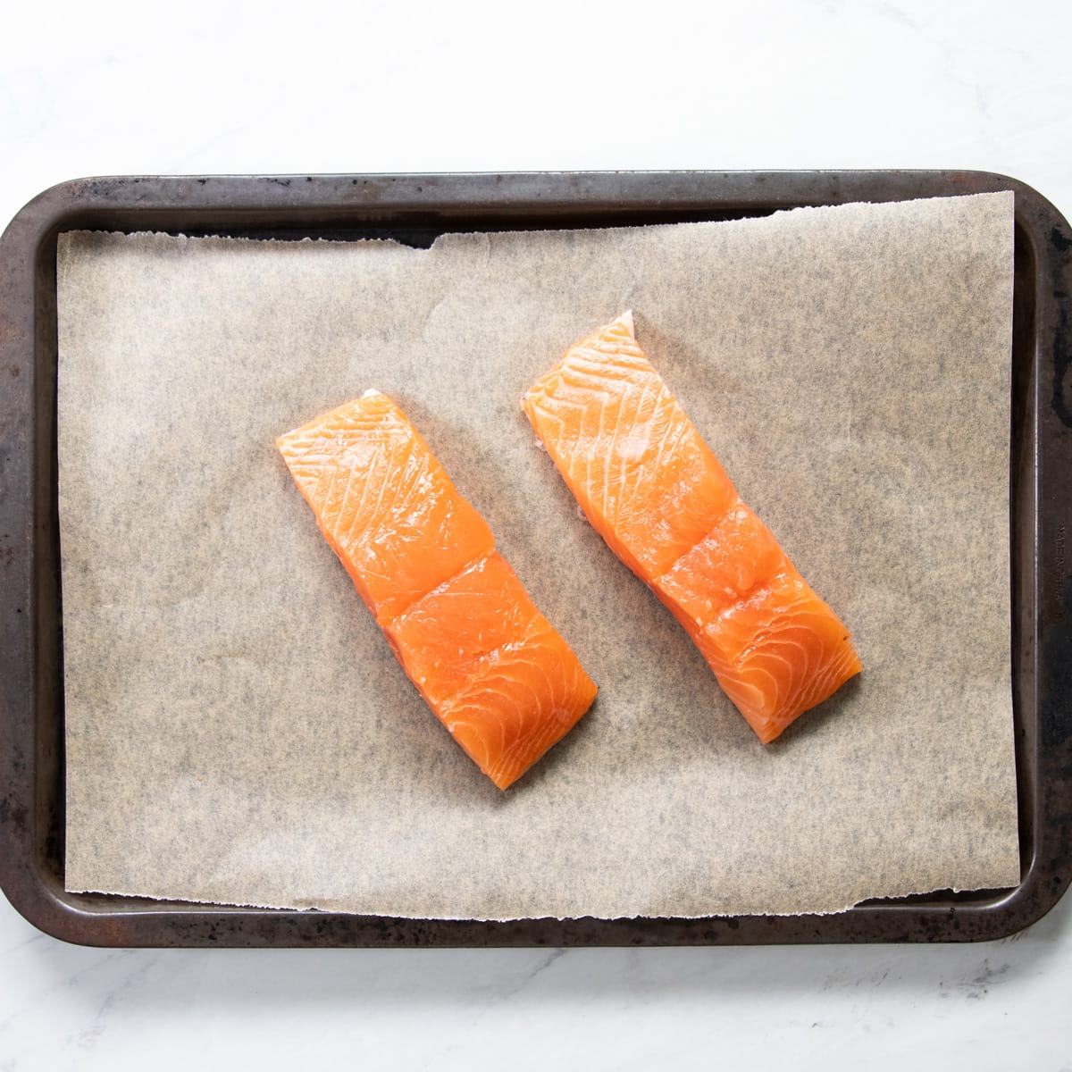 Two raw salmon fillets on a parchment-lined sheet pan.