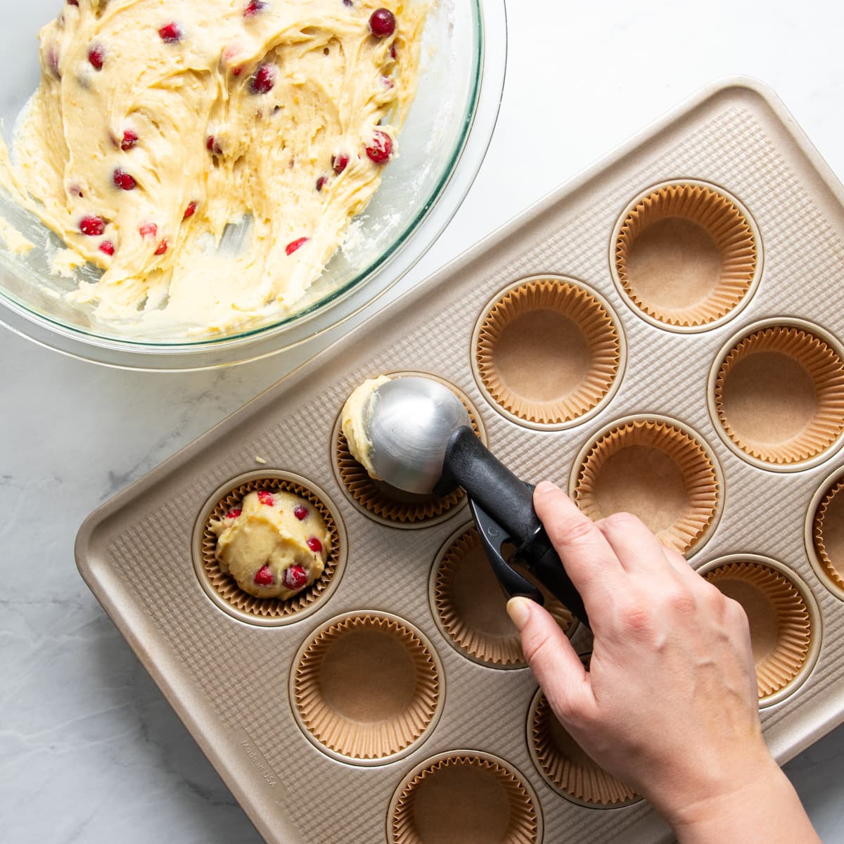 Scooping cranberry-orange muffin batter into a lined muffin tin cup.