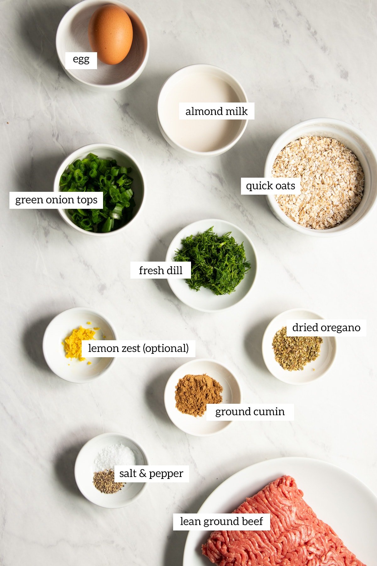 Ingredients needed for low FODMAP Greek Meatballs prepared and measured out into individual dishes on a white marble counter.