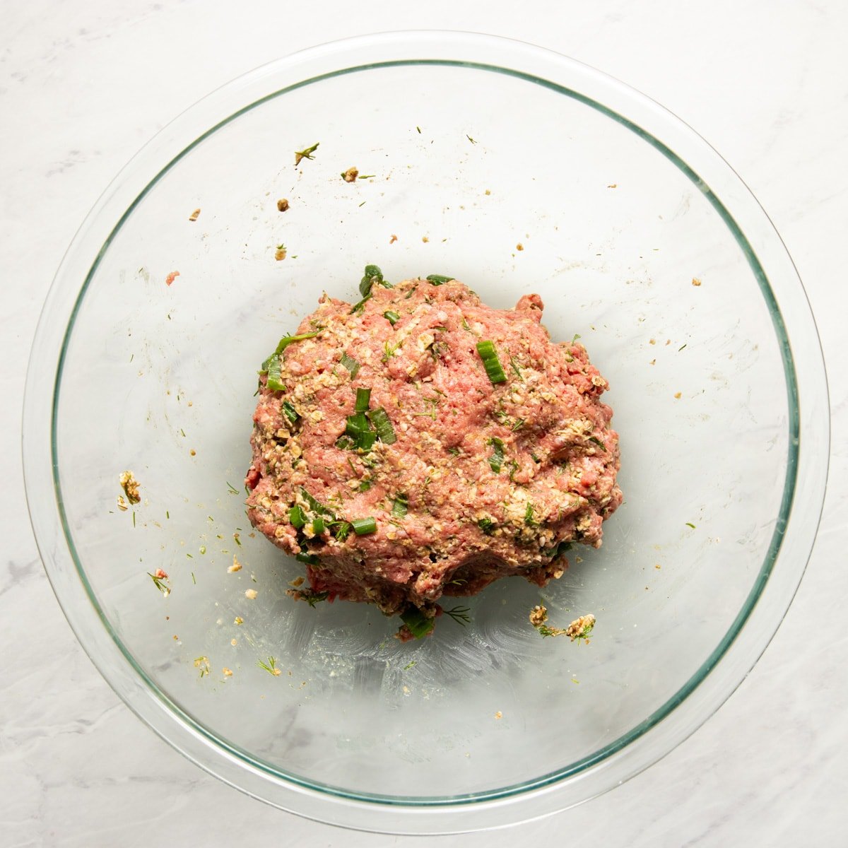 Ground beef mixed with soaked oats, herbs, and spices ready to be rolled into meatballs.