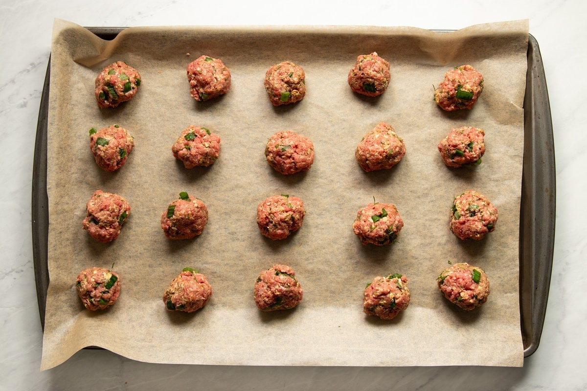 A parchment-lined baking sheet with 20 low FODMAP Greek meatballs rolled and ready to bake in the oven. 