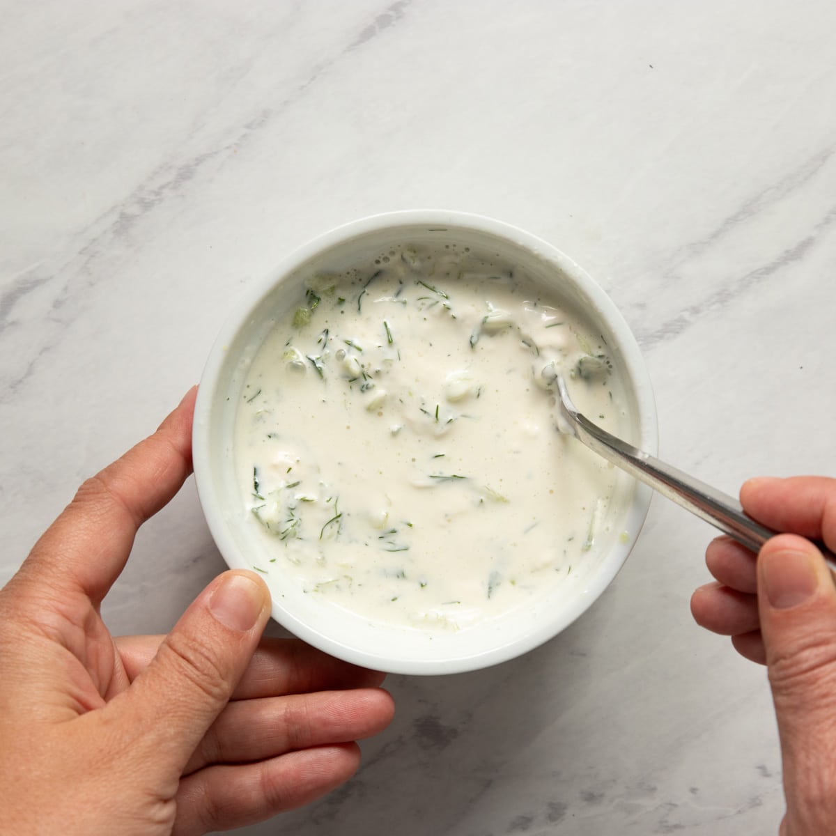 Whisking together a bowl of creamy cucumber dill sauce.