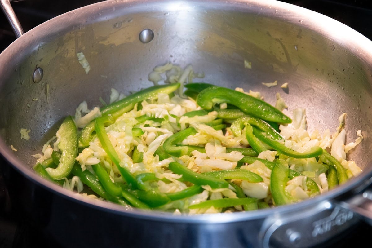 Sauteing green bell peppers and shredded cabbage for pad thai.
