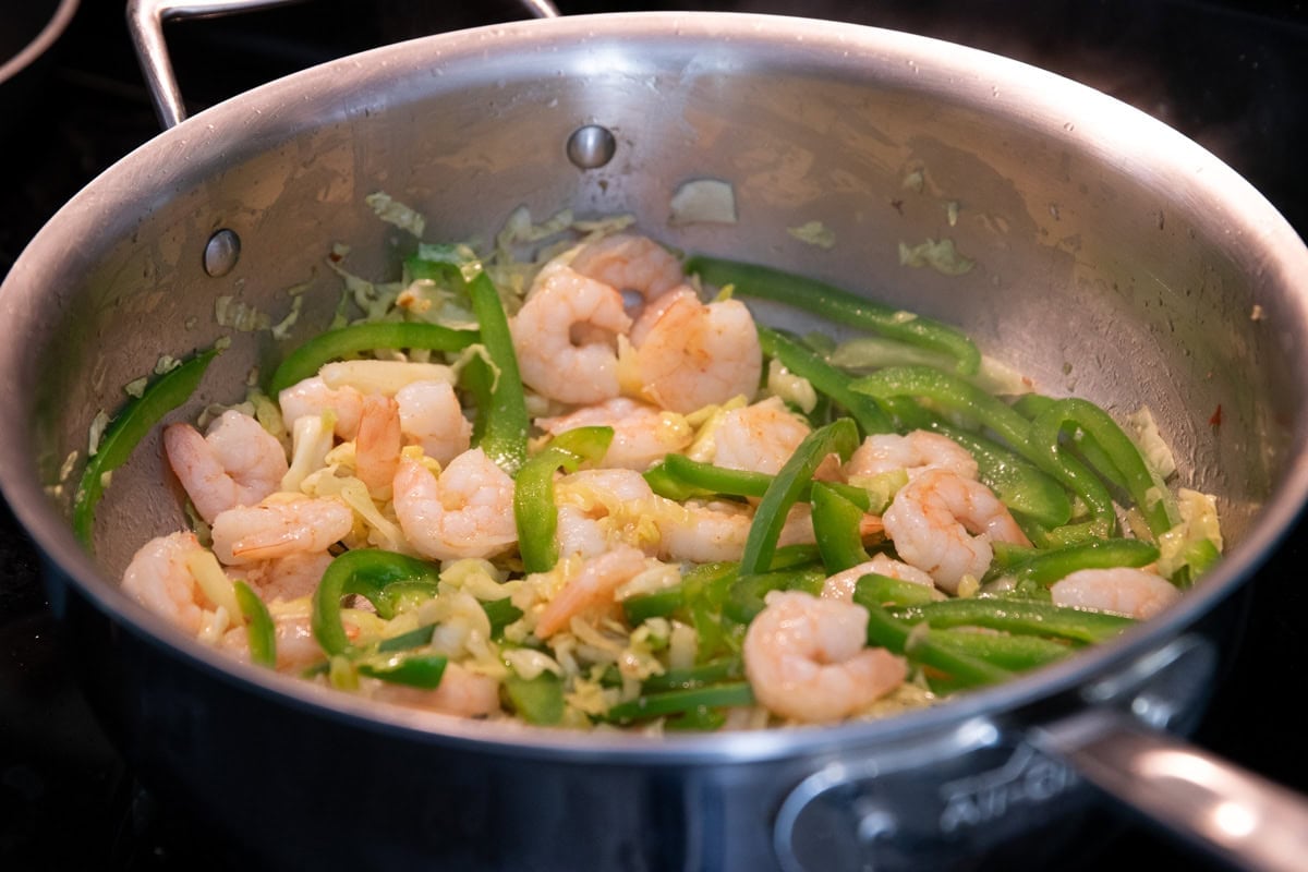 Shrimp has been added to a skillet with sauteed green peppers and cabbage.